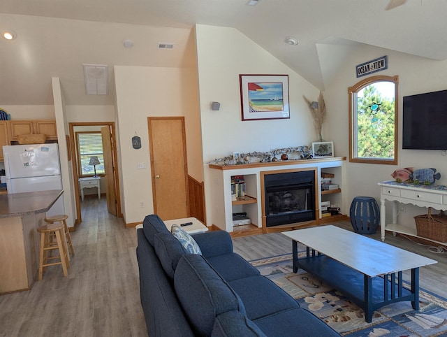 living room featuring vaulted ceiling, a fireplace, visible vents, and light wood-style floors