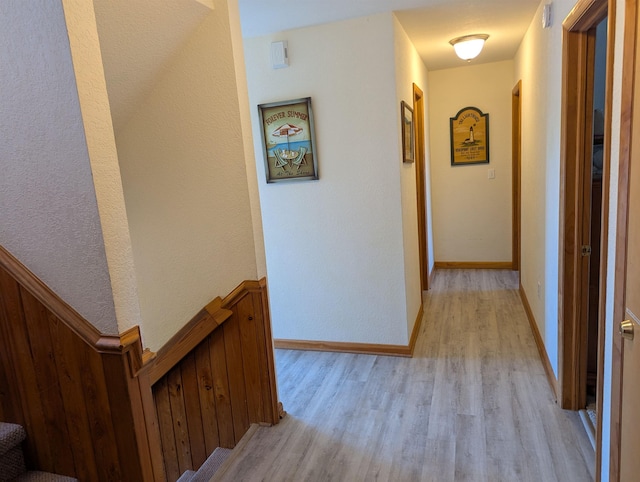 hall with light wood-style floors, baseboards, and stairway