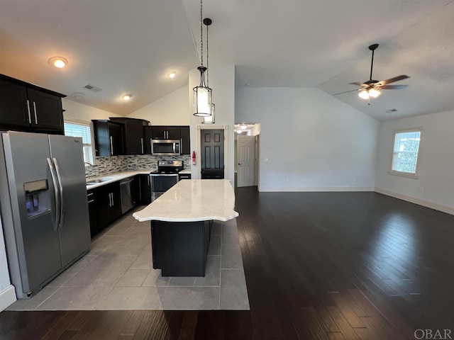 kitchen featuring stainless steel appliances, hanging light fixtures, open floor plan, a kitchen island, and dark cabinets