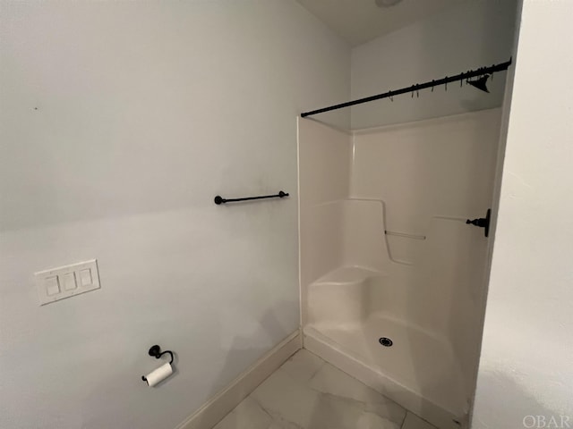 bathroom with marble finish floor, a shower stall, and baseboards