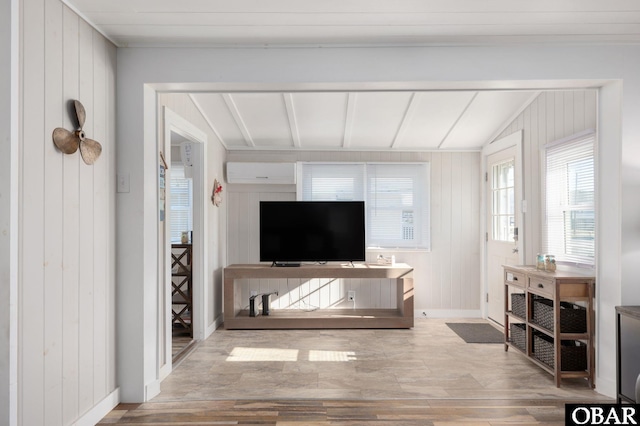 living area with baseboards, a wall unit AC, lofted ceiling with beams, wood finished floors, and wood walls