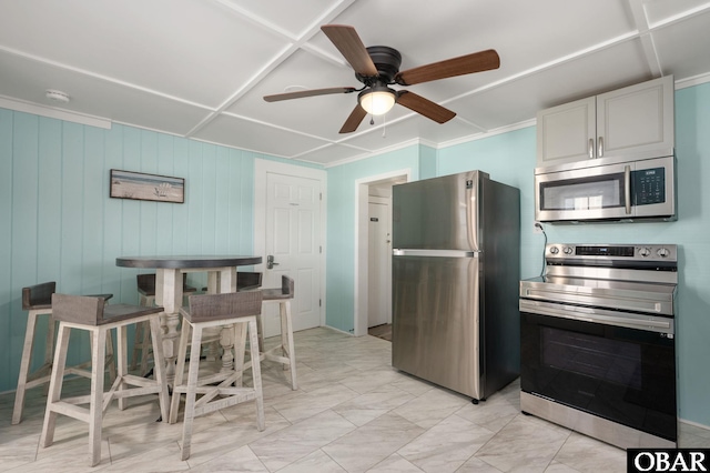 kitchen with stainless steel appliances, white cabinetry, a ceiling fan, marble finish floor, and ornamental molding