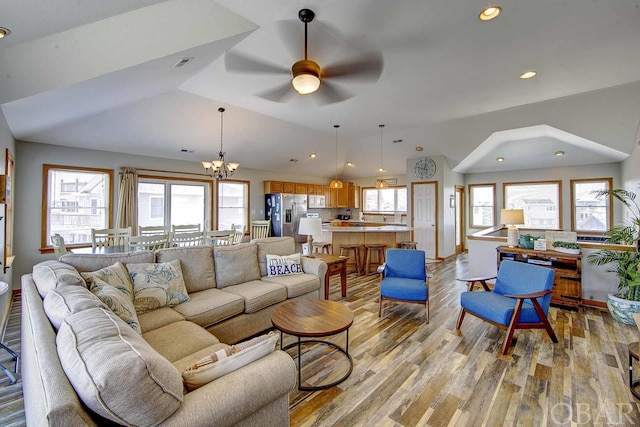 living area with lofted ceiling, recessed lighting, visible vents, light wood-type flooring, and ceiling fan with notable chandelier