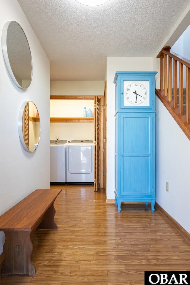 washroom with washing machine and clothes dryer, a textured ceiling, wood finished floors, laundry area, and baseboards