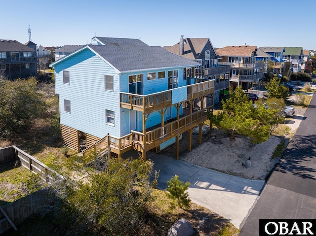 rear view of property featuring driveway, a shingled roof, a residential view, and a balcony