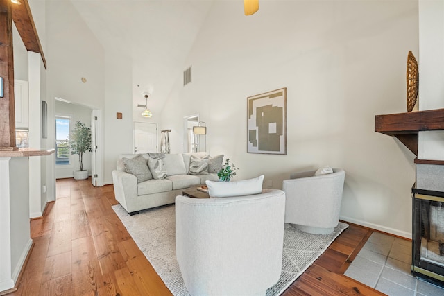 living room with light wood-type flooring, a fireplace, visible vents, and a high ceiling