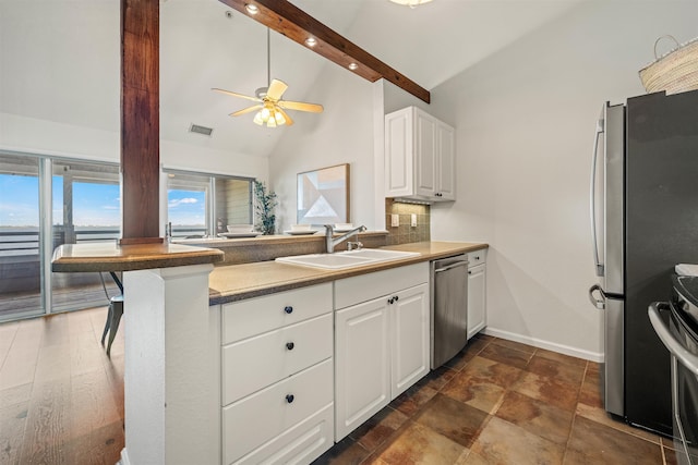 kitchen featuring beam ceiling, appliances with stainless steel finishes, white cabinets, a sink, and a peninsula