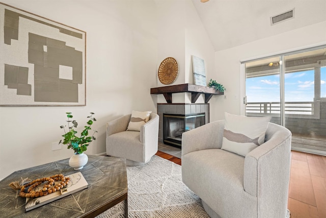 living area with lofted ceiling, visible vents, a tiled fireplace, and wood finished floors