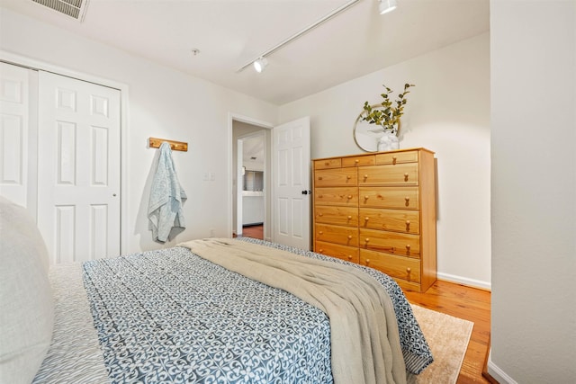 bedroom featuring track lighting, wood finished floors, visible vents, and baseboards