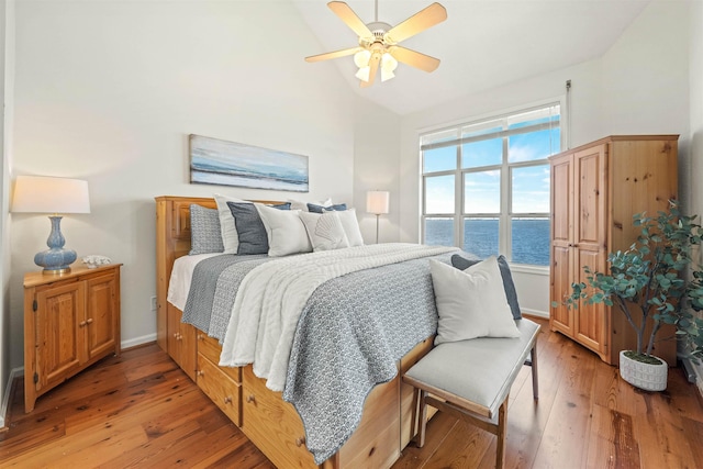 bedroom featuring baseboards, lofted ceiling, ceiling fan, wood finished floors, and a water view