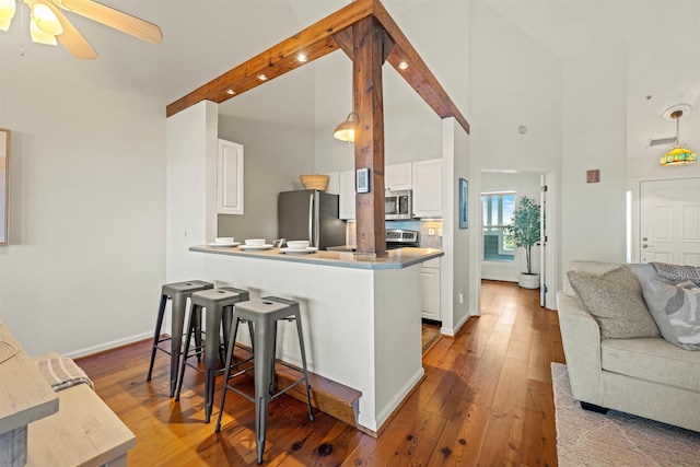 kitchen with a breakfast bar, open floor plan, a peninsula, stainless steel appliances, and white cabinetry