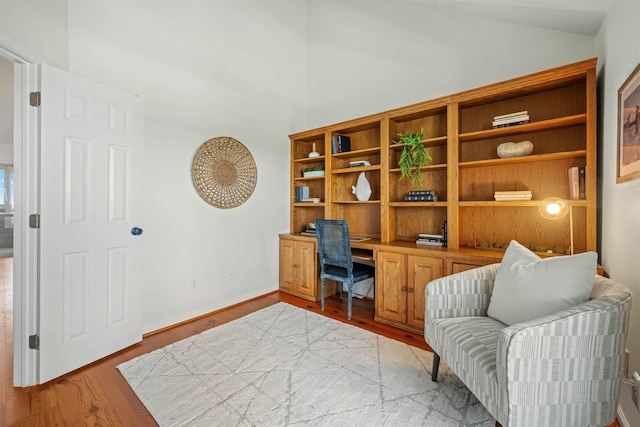 office space with vaulted ceiling, built in desk, and light wood-style flooring