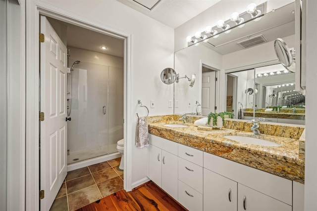 bathroom featuring toilet, a sink, visible vents, and a shower stall