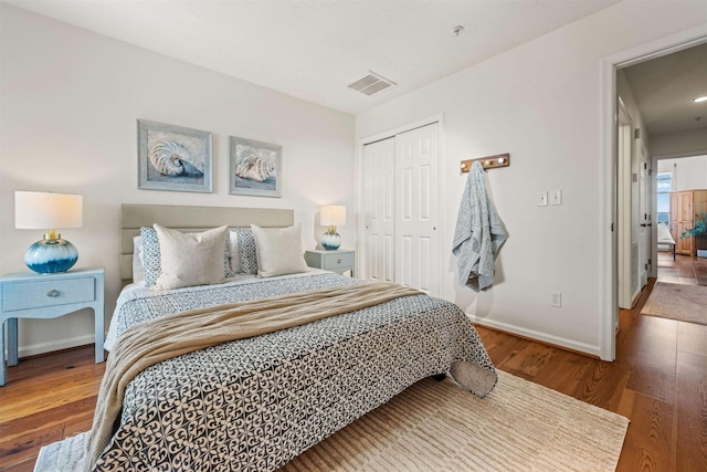 bedroom featuring baseboards, a closet, visible vents, and wood finished floors