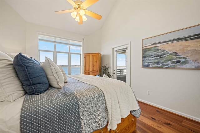 bedroom featuring baseboards, a ceiling fan, wood finished floors, a water view, and high vaulted ceiling