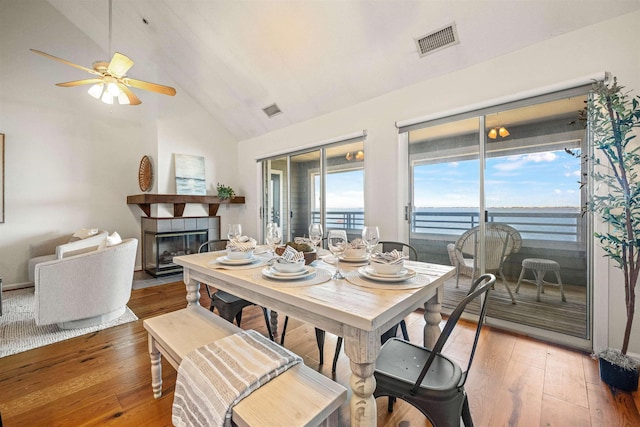 dining space with a tiled fireplace, a water view, wood finished floors, and visible vents