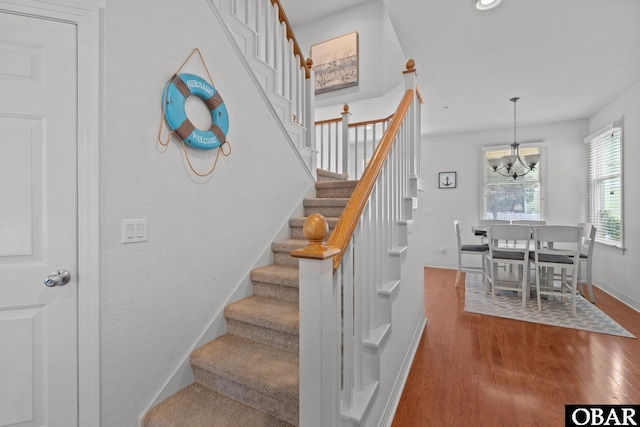 staircase with baseboards, an inviting chandelier, and wood finished floors