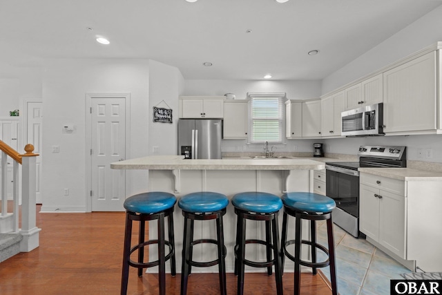 kitchen with a sink, a kitchen breakfast bar, appliances with stainless steel finishes, and white cabinetry