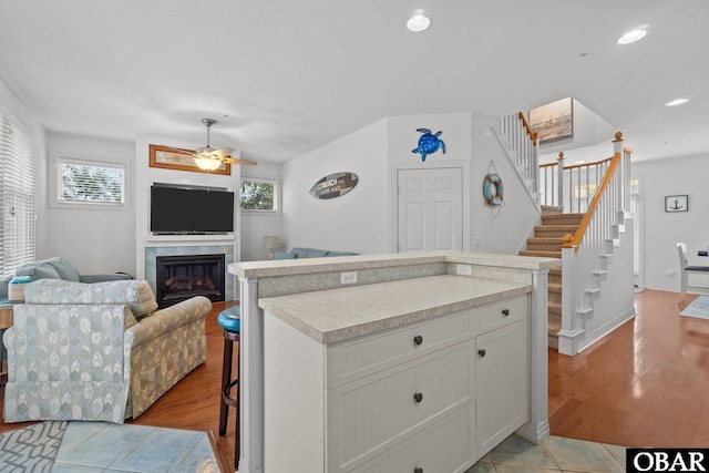 kitchen featuring a ceiling fan, light countertops, a glass covered fireplace, open floor plan, and a center island