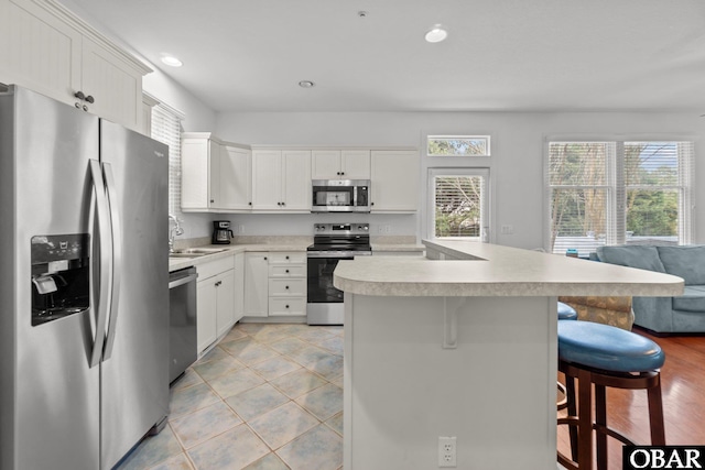 kitchen with a sink, a kitchen breakfast bar, open floor plan, stainless steel appliances, and light countertops