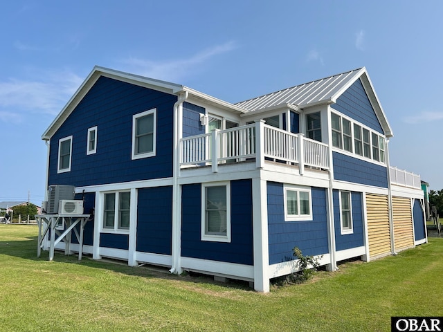 rear view of house with metal roof, a lawn, and a balcony