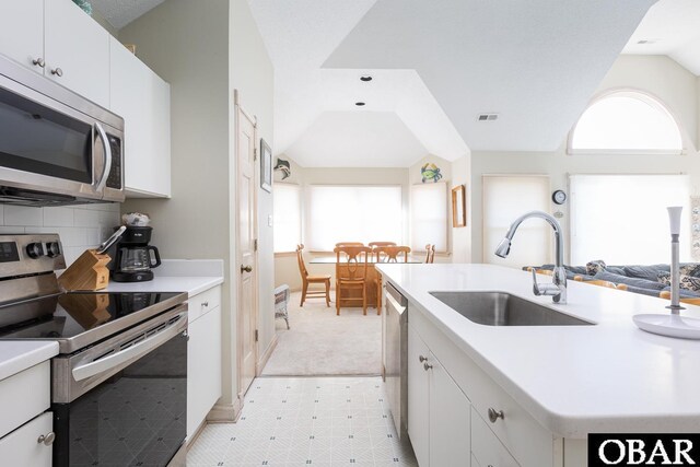 kitchen with stainless steel appliances, light countertops, white cabinetry, a sink, and an island with sink