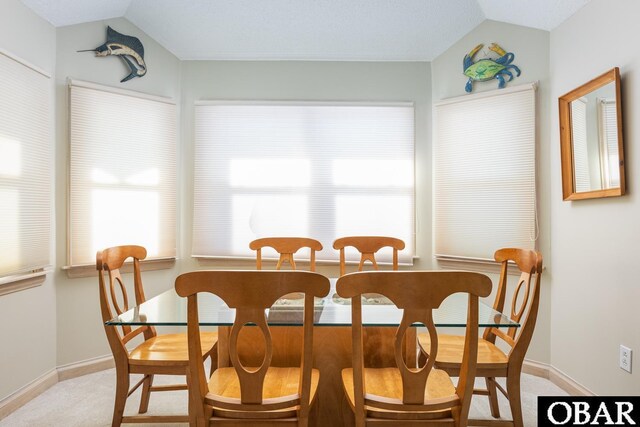 dining space with vaulted ceiling, light colored carpet, and baseboards