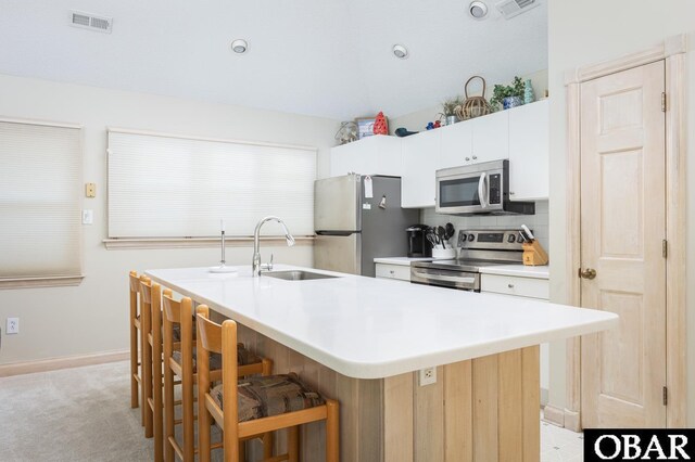 kitchen featuring stainless steel appliances, light countertops, white cabinetry, an island with sink, and a kitchen bar