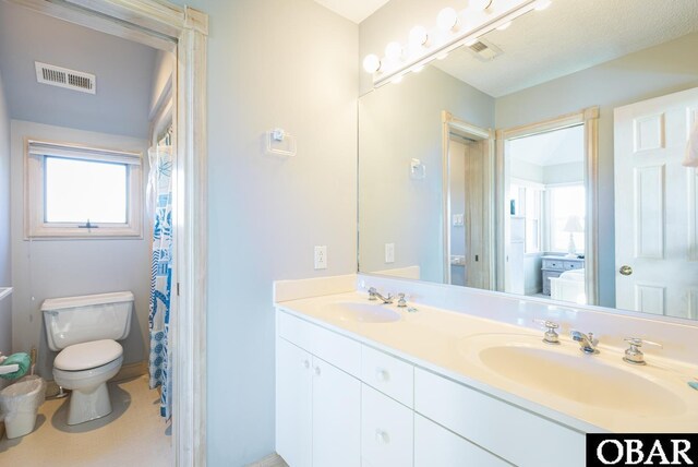 bathroom featuring toilet, double vanity, visible vents, and a sink