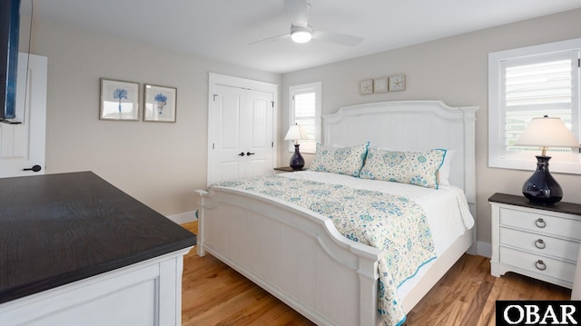 bedroom with light wood-type flooring, ceiling fan, baseboards, and a closet