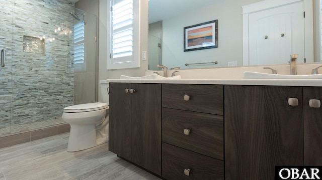 full bathroom featuring double vanity, a stall shower, a sink, and toilet