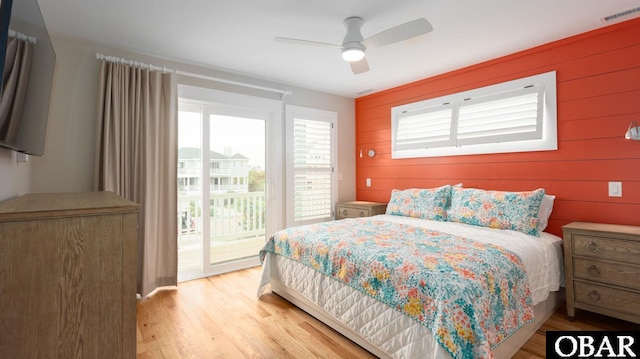 bedroom with access to exterior, visible vents, a ceiling fan, wood walls, and light wood-type flooring