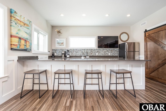 kitchen featuring tasteful backsplash, freestanding refrigerator, a kitchen bar, and a barn door