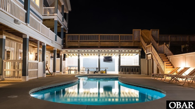 pool at night with stairway, a patio area, and a community pool