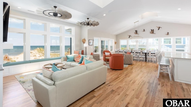 living area with high vaulted ceiling, a skylight, a water view, and light wood-style flooring