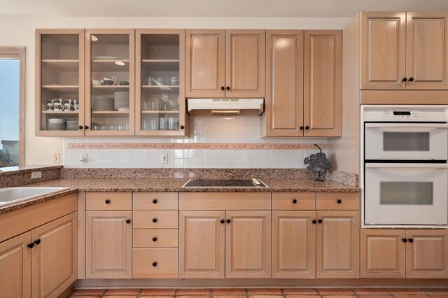 kitchen with glass insert cabinets, double oven, light brown cabinets, under cabinet range hood, and black electric cooktop