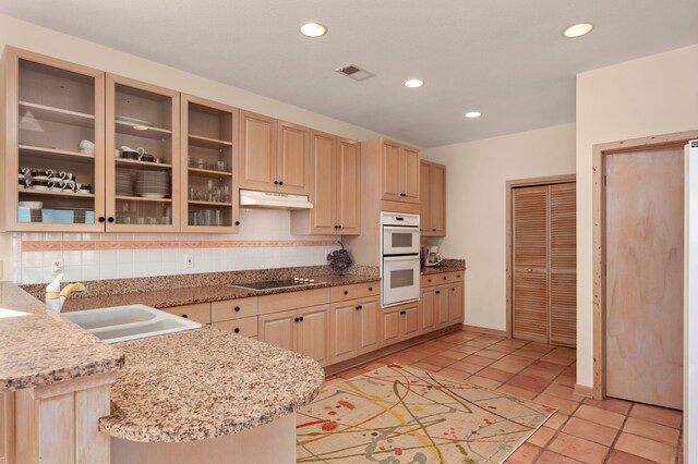 kitchen with a sink, a peninsula, light brown cabinets, and glass insert cabinets