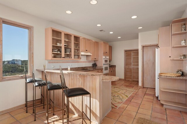 kitchen with glass insert cabinets, a peninsula, under cabinet range hood, a kitchen bar, and open shelves