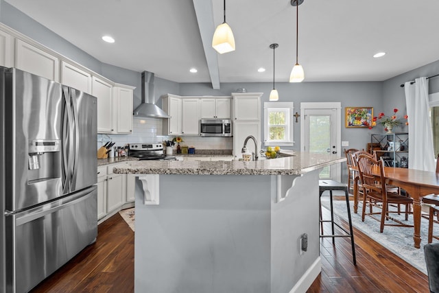 kitchen with hanging light fixtures, wall chimney range hood, appliances with stainless steel finishes, and white cabinets