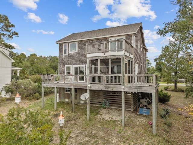 rear view of property featuring a shingled roof, a sunroom, a deck, and a carport