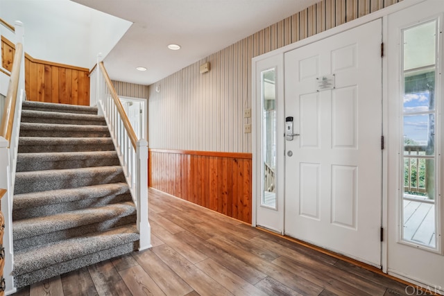 foyer entrance with wallpapered walls, a wainscoted wall, wood finished floors, stairs, and recessed lighting