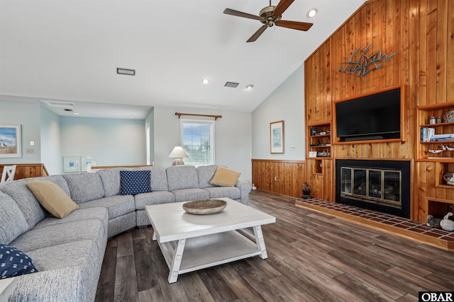 living room with high vaulted ceiling, wood walls, dark wood finished floors, visible vents, and a glass covered fireplace