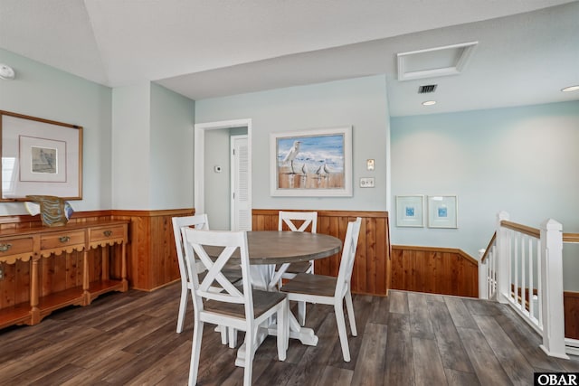 dining space with a wainscoted wall, dark wood finished floors, visible vents, attic access, and wooden walls