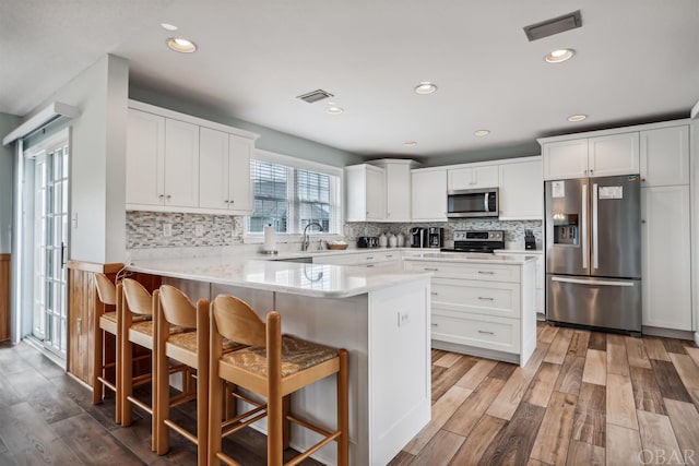 kitchen with appliances with stainless steel finishes, white cabinetry, a peninsula, and a kitchen breakfast bar