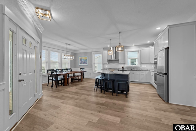 1207 Tail Wind Ct Lot 267, Corolla, NC 27927 - kitchen with wall chimney exhaust hood, crown molding, light wood-style flooring, a breakfast bar area, and freestanding refrigerator