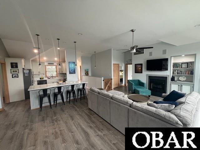 living room with built in features, a ceiling fan, lofted ceiling, a fireplace, and light wood-style floors