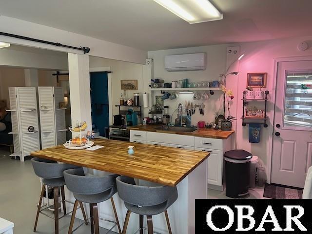 kitchen with a breakfast bar area, a sink, an AC wall unit, white cabinets, and butcher block counters