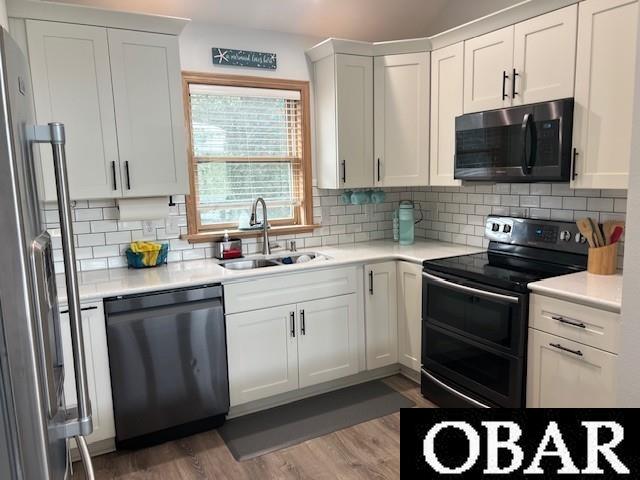 kitchen featuring light wood-type flooring, a sink, white cabinetry, stainless steel appliances, and light countertops