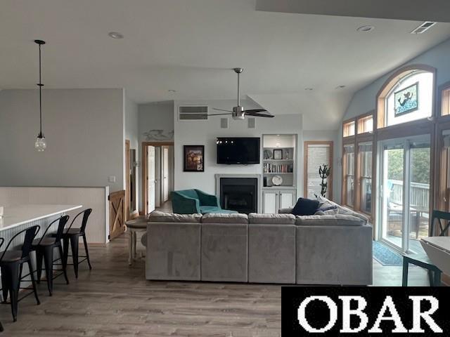 living room with built in shelves, visible vents, light wood finished floors, a fireplace, and vaulted ceiling