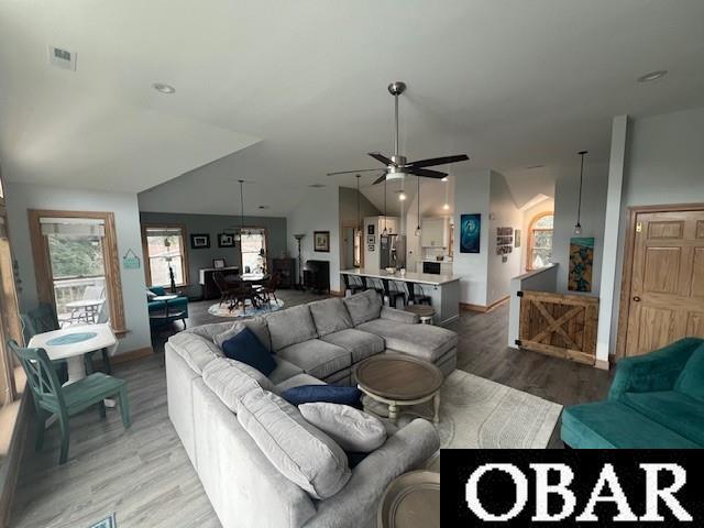 living area with a ceiling fan, visible vents, light wood finished floors, baseboards, and vaulted ceiling